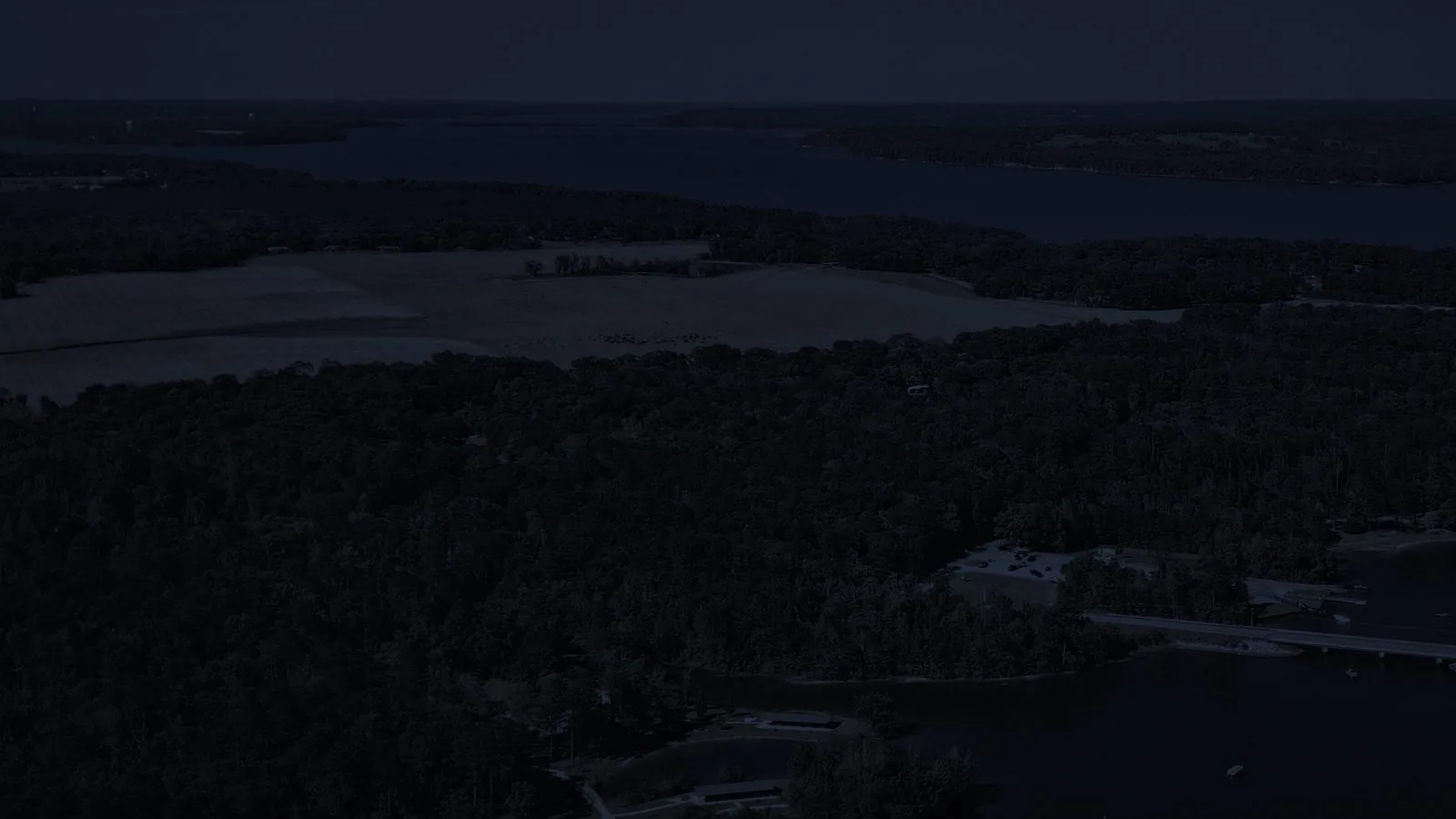 Near-black aerial of night woods and water, almost nothing visible to the eye